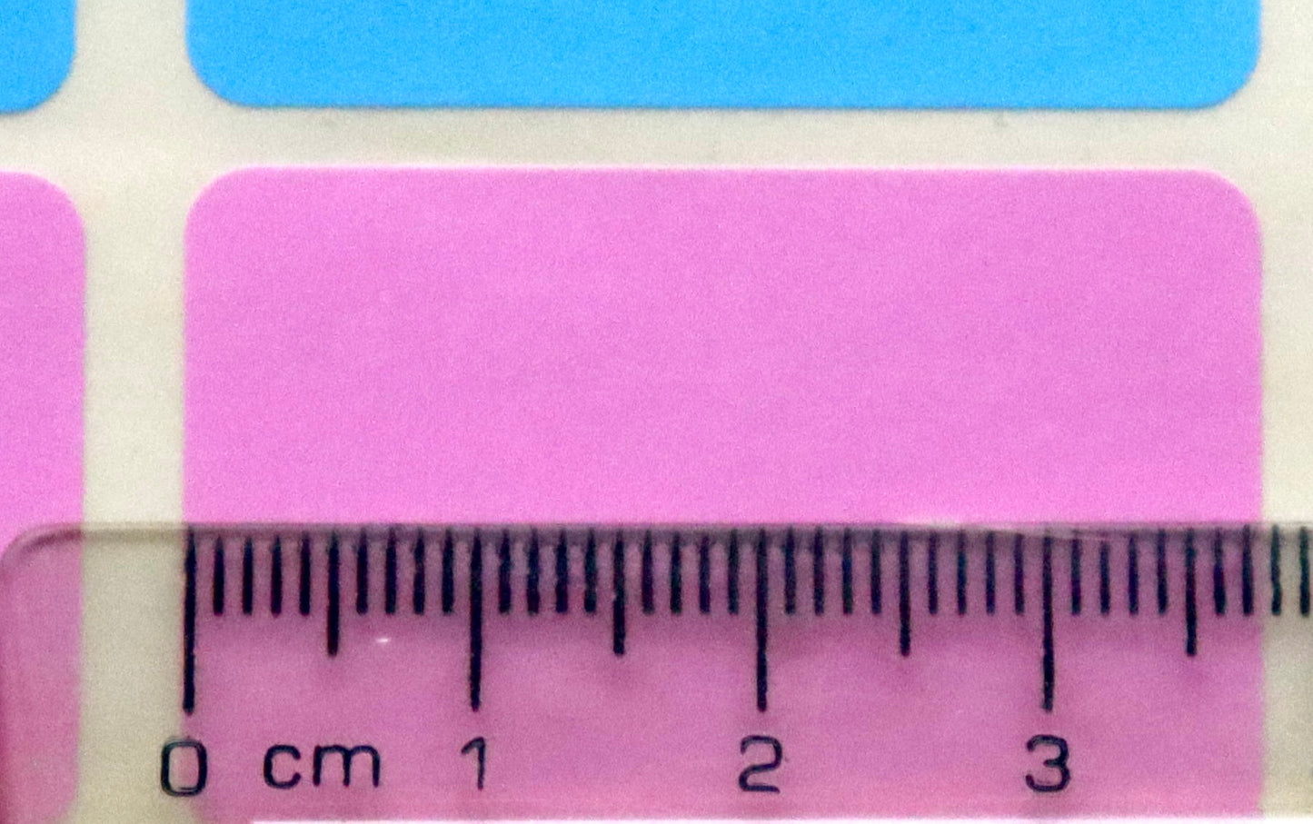 A clear ruler measures a pink rectangular sticker, which is approximately 3.8 cm wide.