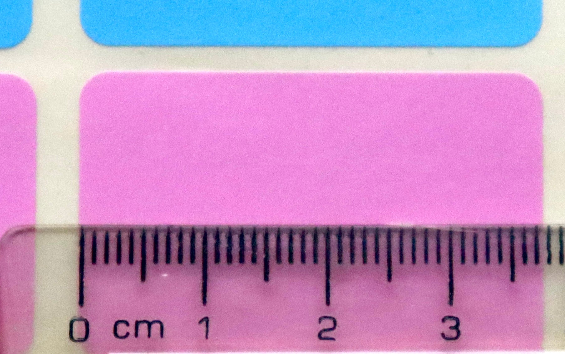 A clear ruler measures a pink rectangular sticker, which is approximately 3.8 cm wide.