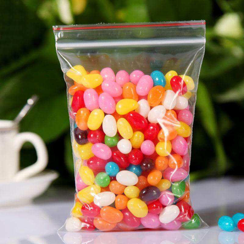 Clear bag filled with colorful jelly beans on a blurred natural background